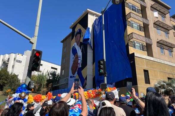 A crowd gather in front of a mural on the side of a building.