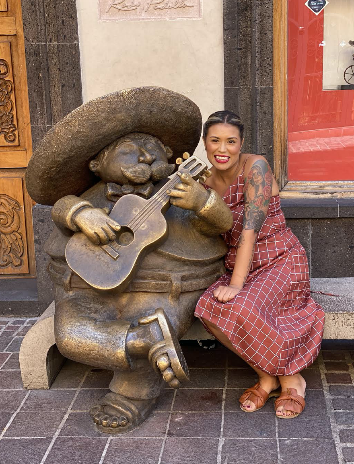 Flor sits one a bench next to a bronze sculpture of a cartoon-like man playing a guitar.