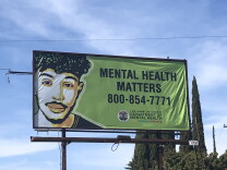 A billboard with a green background and the illutration of a mustachioed man reads: MENTAL HEALTH MATTERS 800-854-771