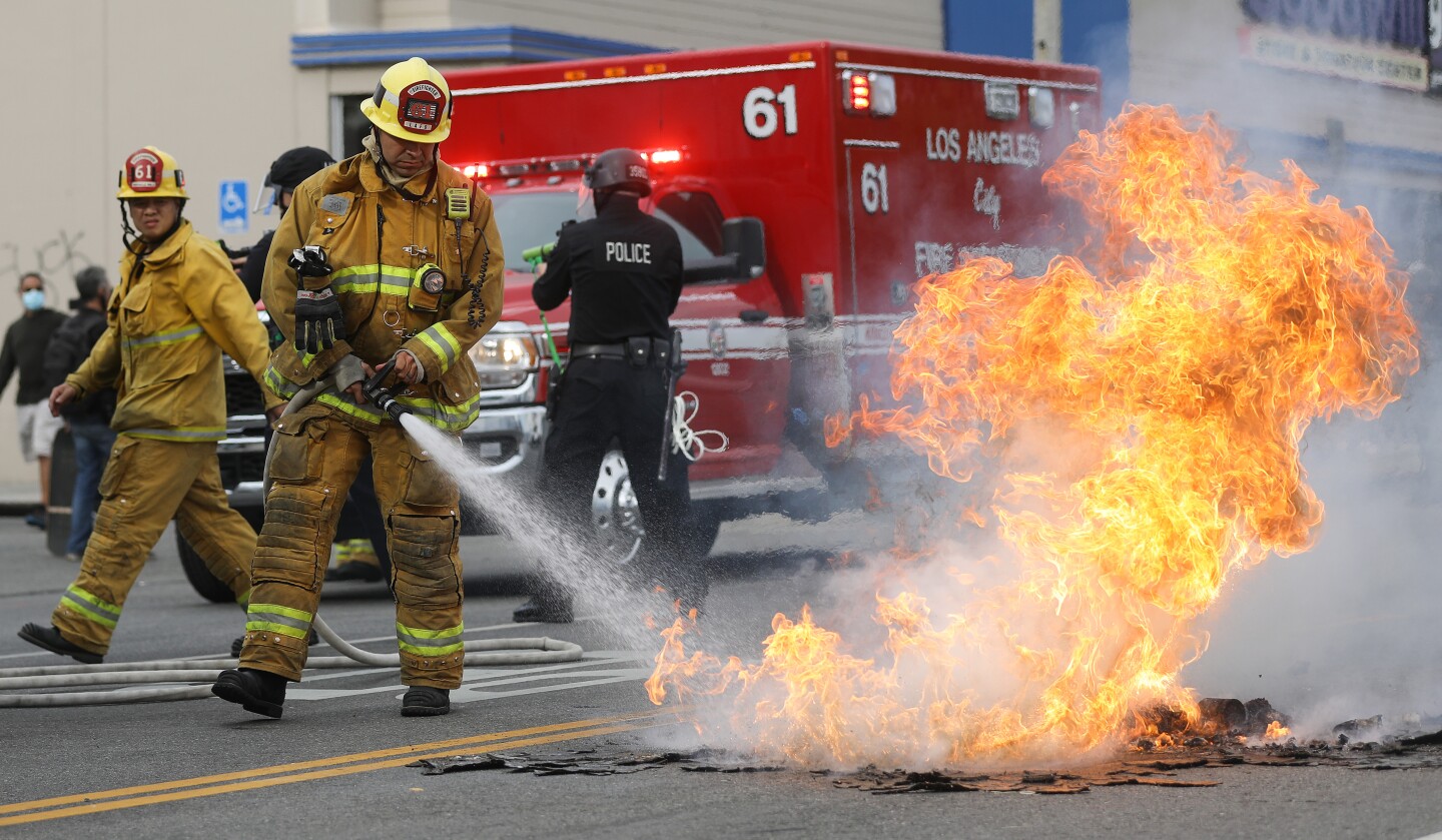 An image of a firefighter uses a water hose to put out a fire engullfing some unidentified material on the street