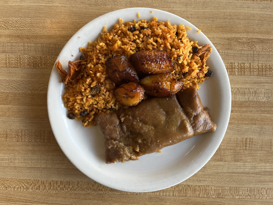 Puerto Rican pasteles, a local version of a tamale, sits on a white plate next to a helping of rice and fried plantains