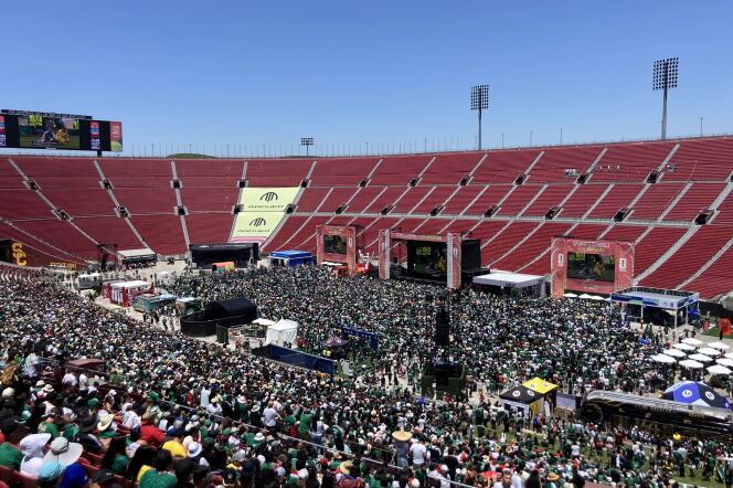 A large crowd of people inside a stadium with multiple large screens. 