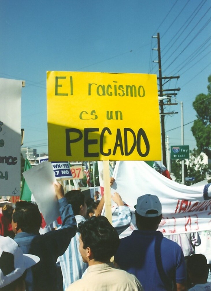 A handmade yellow poster reads: "El racismo es un pecado"
