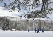 People in blue snow jackets and dark stand in a snowy field with instruments