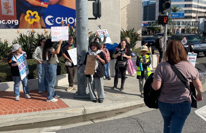 Protesters on a street corner hold signs with slogans that include "Politicians should not make healthcare decisions," "Patients before politics" and "Trust doctors."
