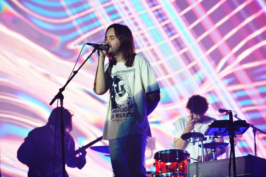 The band Tame Impala performs under streaky pink, purple, blue, and yellow lighting designs.
