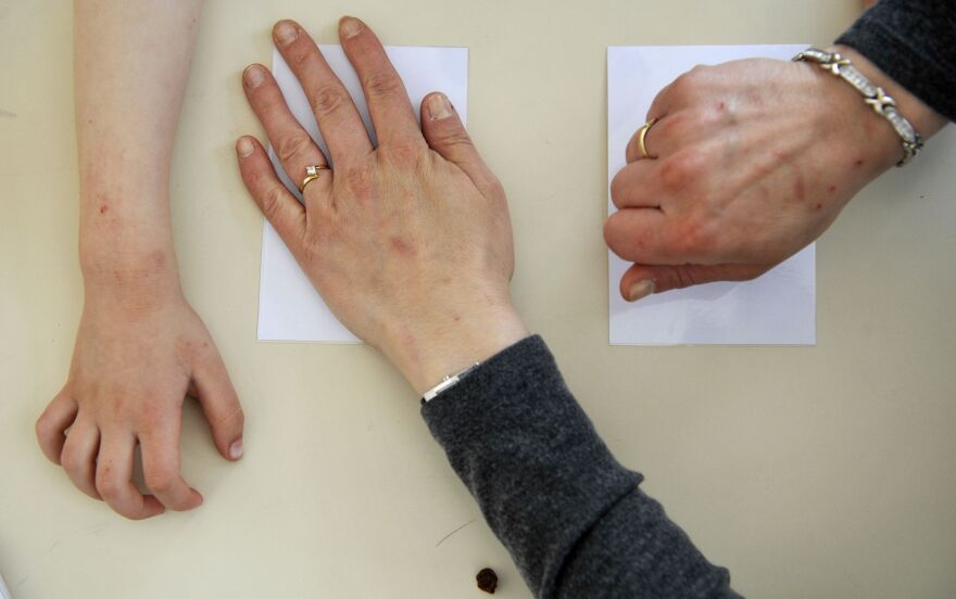 A photo depicting 3 hands. Two hands, belong to an adult, separately cover two sheets of paper. A child's hand can be found off to the side of the two.