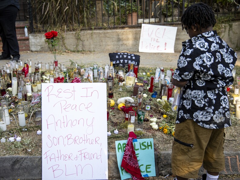Signs read Rest in Peace Anthony Son Brother Father Friend BLM at a makeshift memorial with candles and flowers.
