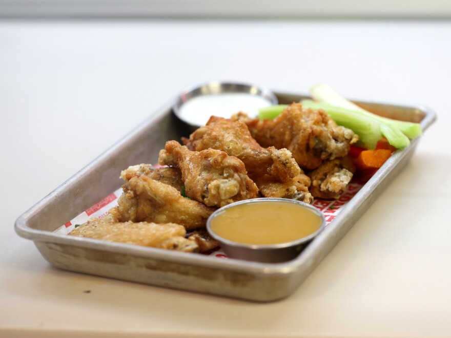 An order of buffalo chicken wings, a side of mustard-colored dipping sauce, celery and carrots on a metal tray sits on a counter.