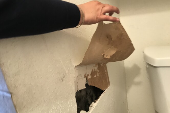 A woman points out for a large hole in the walls of her apartment.
