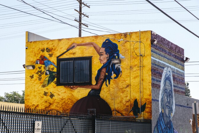 "Decolonized" a mural painted by Kristy Sandoval in Pacoima depicts a woman with blue hair releasing birds from a cage on the side of a yellow building