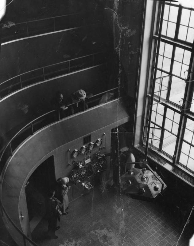 A black and white photo shows two people peering down from the stadium seating inside an operating room at LA's old general hospital.