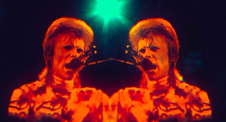 Mirror images of David Bowie with a circle design on his forehead, lit in red with a green light in the background.