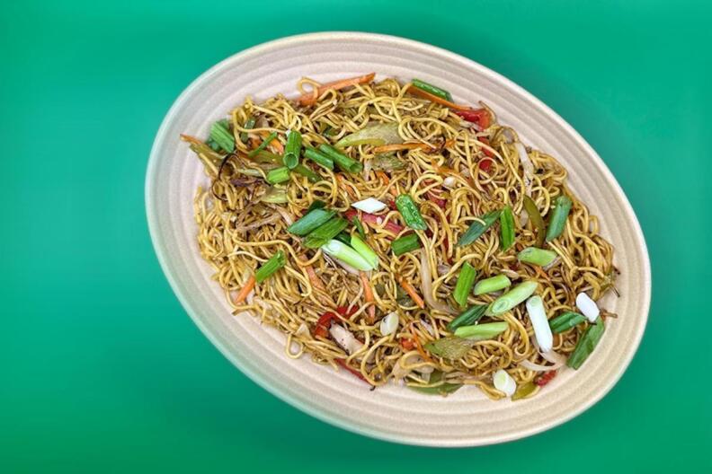 A plate of garlic noodles with green onions on a white plate on a green table.