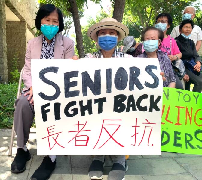 Six Asian seniors, five of them women, hold signs. A large sign in the forefront reads “Seniors Fight Back” in English and Chinese.