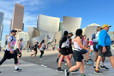 Runners and walkers running past a silver building in odd shape