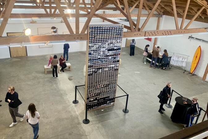 People surround a "tower" of images in a large art gallery space.