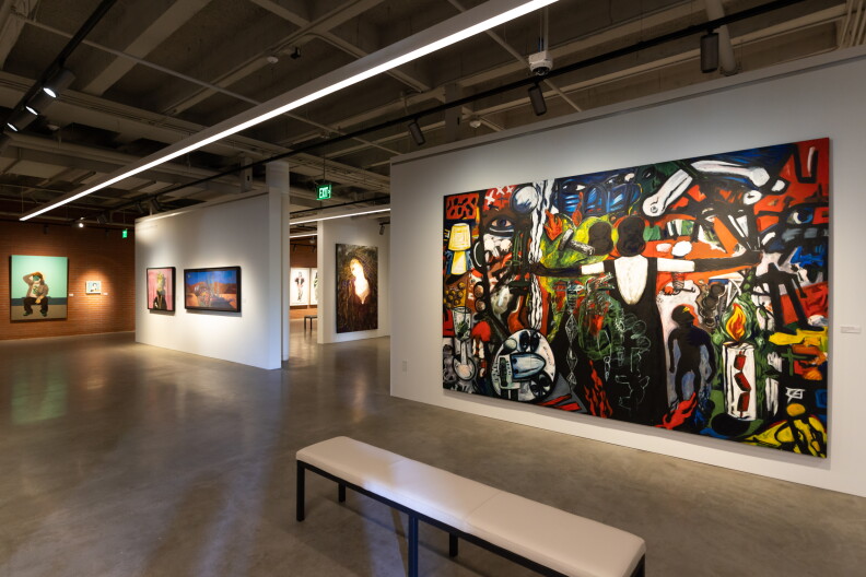 A large, horizontal, colorful piece with dark figures at the center hangs on a wall, other art on other walls in the background.