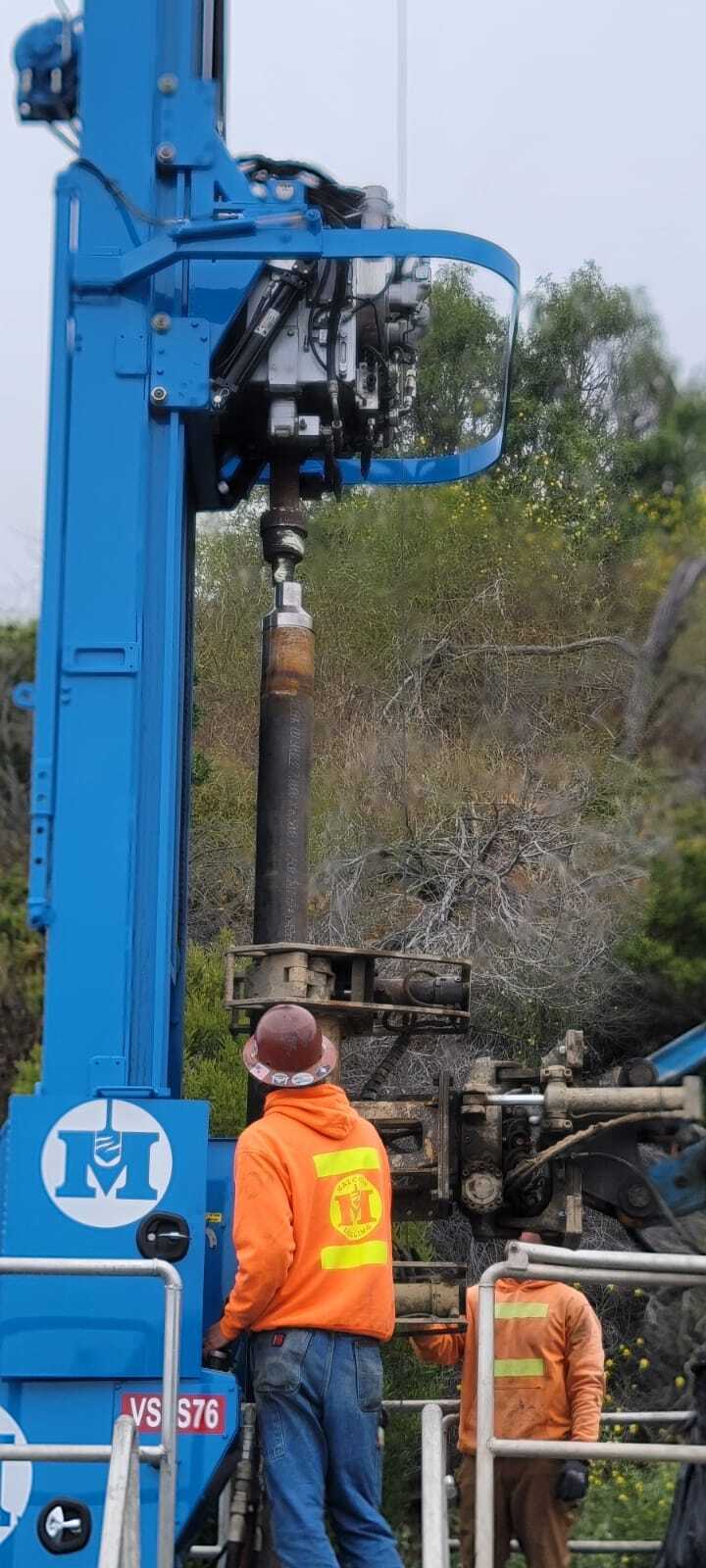 Workers in red helmets and orange sweatshirts with a big machine.