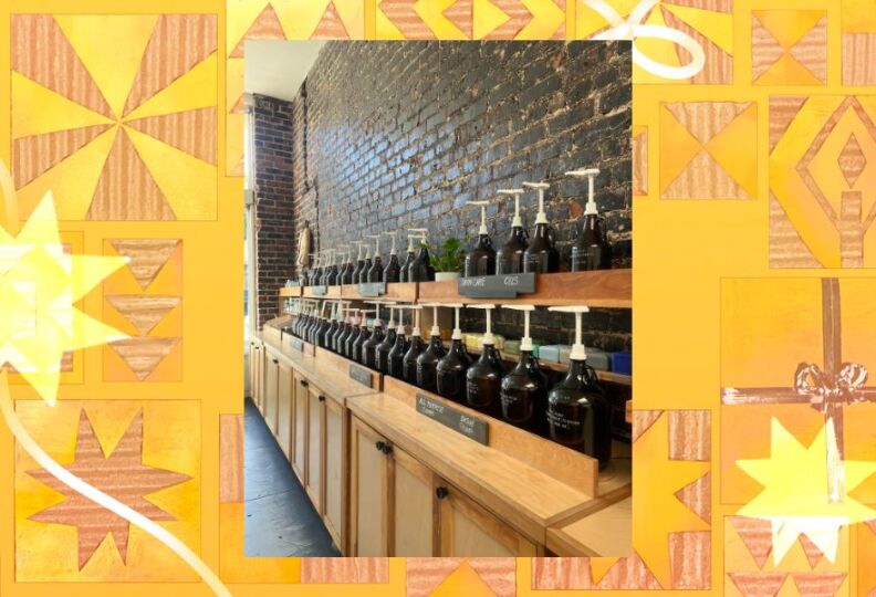 The interior of a shop, with wood shelving lined up against a dark brick wall: Atop the shelves are several pump containers and labels. The photo is set against a festive gold background accented with images of stars, gift boxes and ribbons.