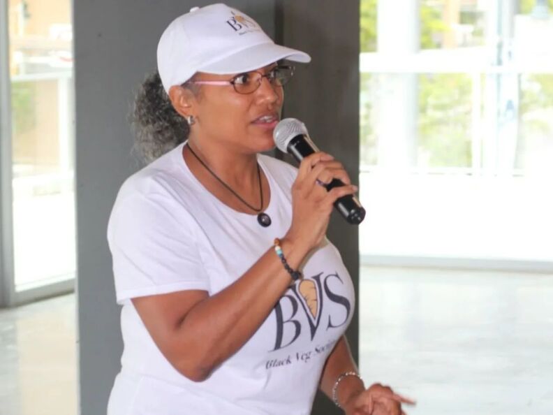 A woman holds a mic and wears a white cap.