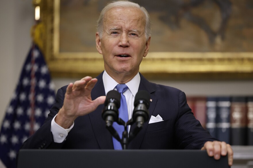 President Biden stands at a lectern with his hand raised and a U.S. flag behind him.