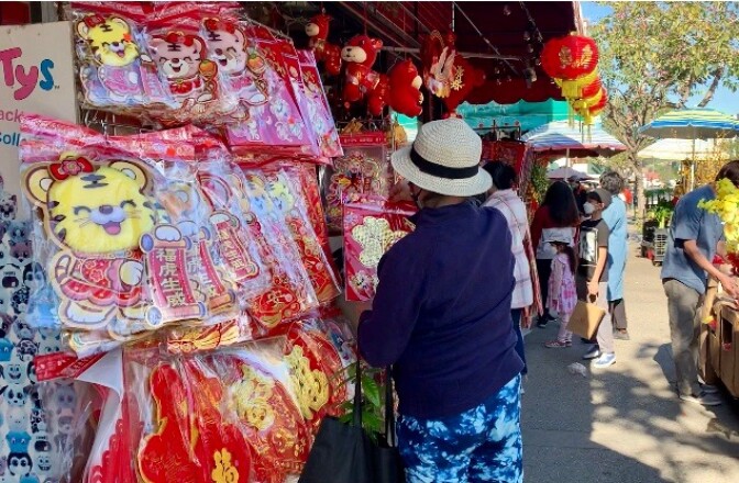 A woman in a hat, her back to the camera, browses Lunar New Year decorations on a busy street. 