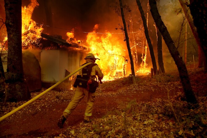 MAGALIA, CA - NOVEMBER 09: A Cal Fire firefighter pulls a hose towards a burning home as the Camp Fire moves through the area on November 9, 2018 in Magalia, California. Fueled by high winds and low humidity, the rapidly spreading Camp Fire ripped through the town of Paradise and has quickly charred 70,000 acres and has destroyed numerous homes and businesses in a matter of hours. The fire is currently at five percent containment. (Photo by Justin Sullivan/Getty Images)
