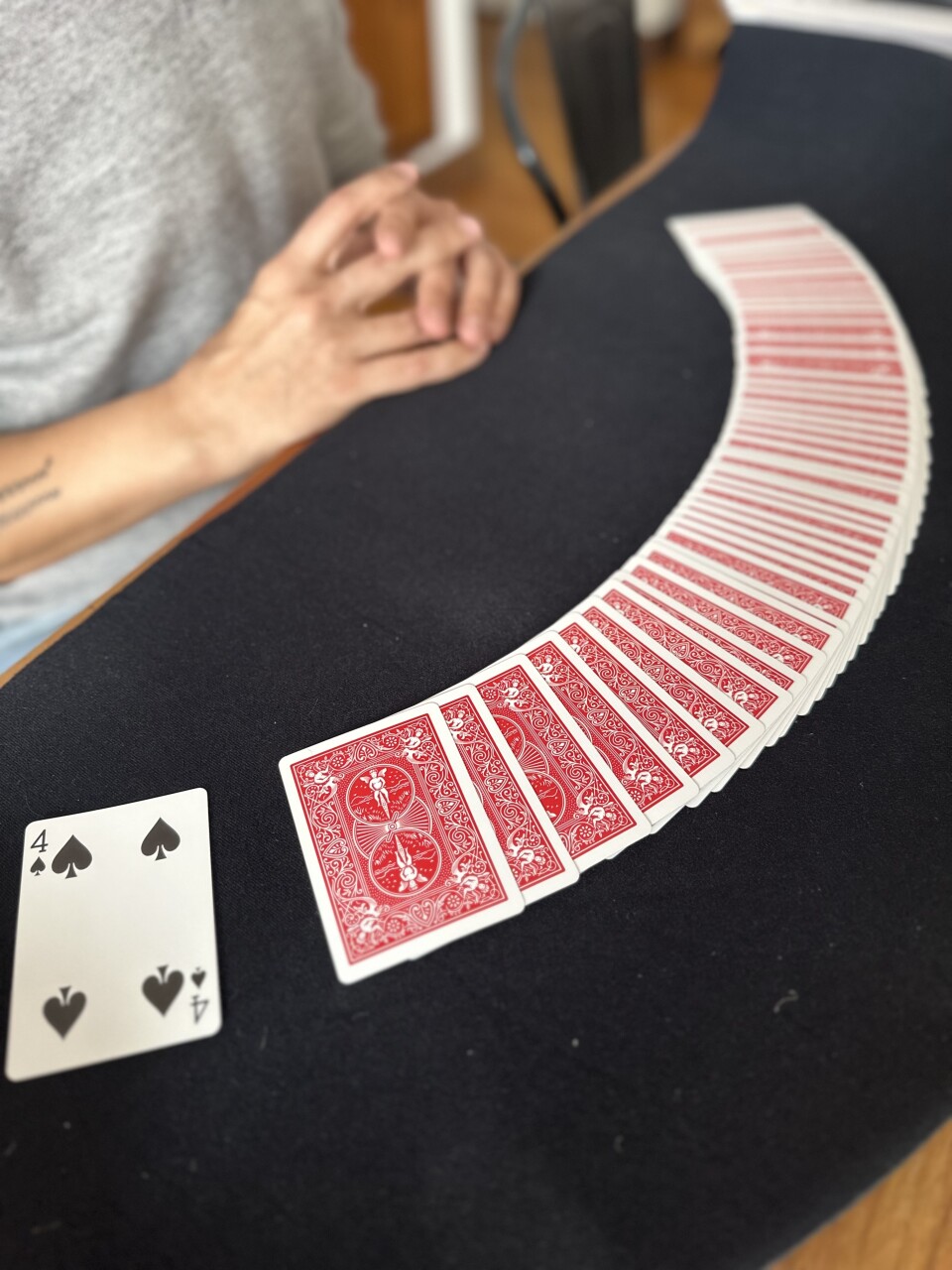 A deck of cards with red backing spread out on a black felt table. All are face down except the 4 of clubs