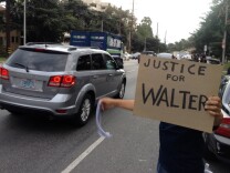 A man hold a sign and waves a rag in support of Walter DeLeon, who was unarmed when an LAPD officer shot and critically wounded him June 19.