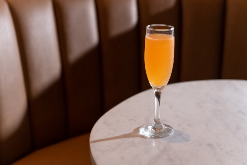 A champagne glass filled with orange liquid sits on top of a white marble tabletop.