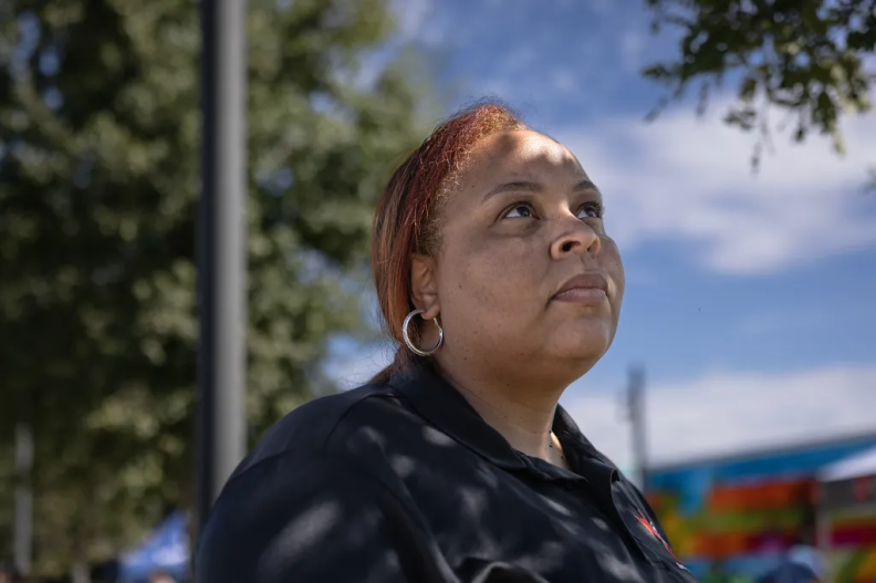 A woman with light brown skin and red-tinted hair stares into the distance