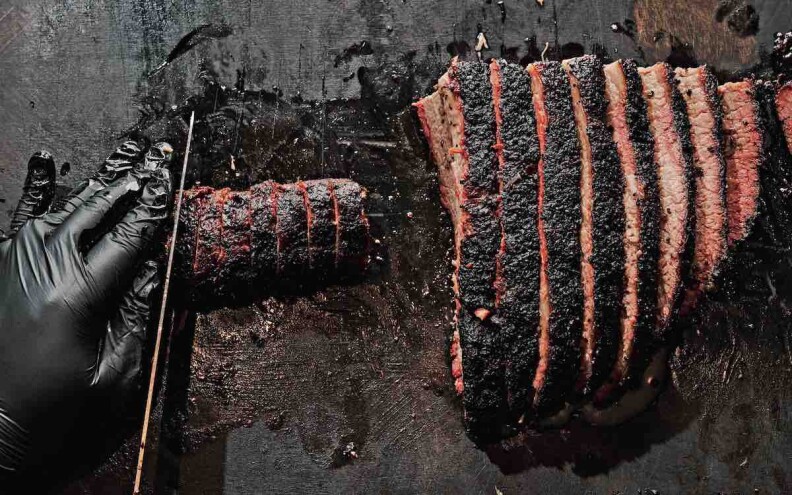 Horn Barbecue's brisket being cut by a gloved black hand and knife.