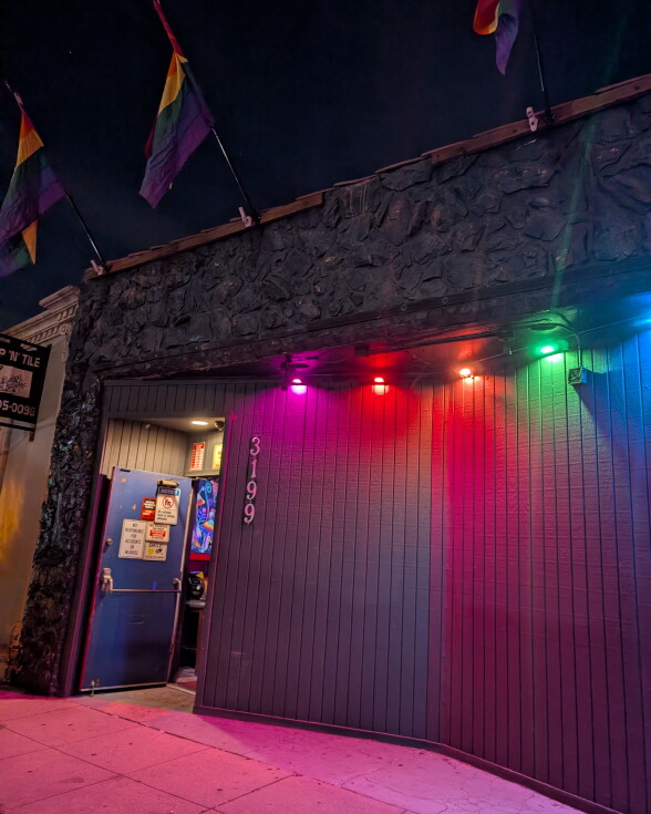 Exterior of a LGBTQ+ bar. Rainbow flags are hanging from the building. And rainbow color lights.