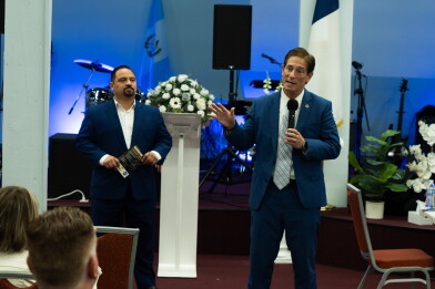A man with a microphone speaks in a church building to a crowd.