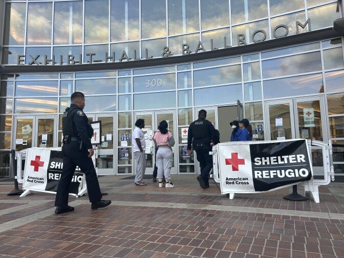 Police walk into a large building marked with banners that read "American Red Cross Shelter" 