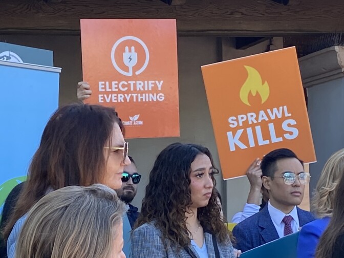 A close-up of a small group of people, two of them holding signs that say "Electrify Everything" and "Sprawl Kills."