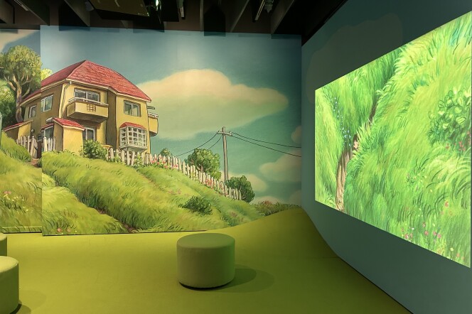 A corner of a room with grass-green carpet and round stools in the same color. The left wall is covered in a mural of a yellow home on a grassy hill. The right wall is showing a clip from the movie Ponyo featuring bright green animated grass.