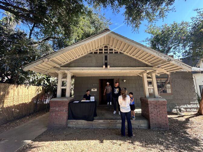 The front patio of a single-story home. The grass is dry and brown, and five people are standing near the front door.