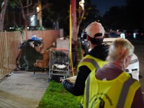 Two people wearing reflective vests stand next to a makeshift shelter on the sidewalk.