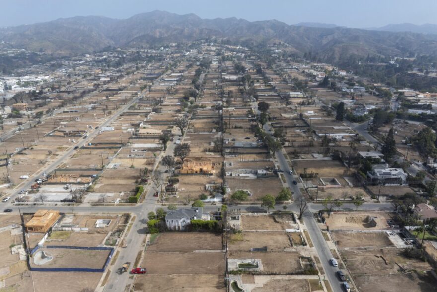 Aerial view of mostly empty residential lots where homes were burned during a wildfire. A mountain range is pictured in the background.