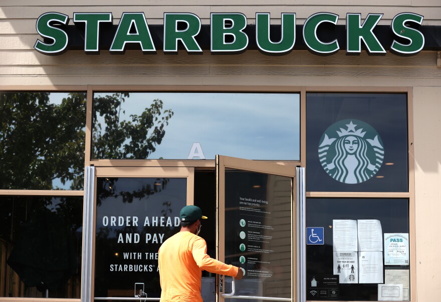 A person opens a door to walk into the store. A sign with green lettering overhead reads "Starbucks."