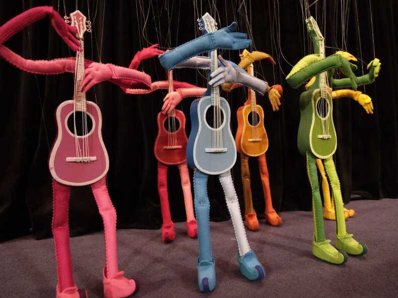 Five marionette guitars play of different colors perform on a stage.