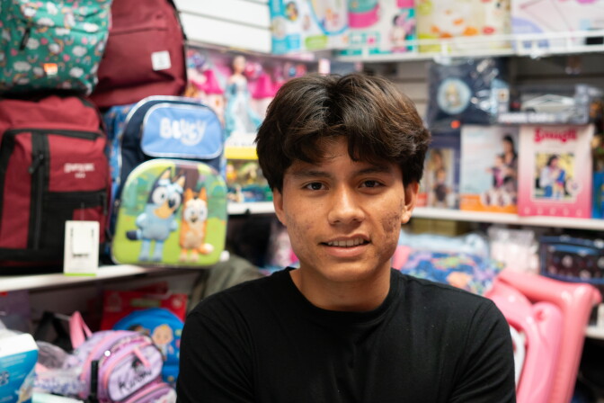A young man stands in front of a vendor stand full of backpacks for sale.