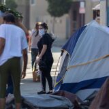 LOS ANGELES, CA - MAY 08: A flower buyer looks back to a homeless woman and her sidewalk encampment as businesses in the flower district in Skid Row reopen in time for Mother's Day on May 8, 2020 in Los Angeles, California. Local stay-at-home restrictions are being relaxed to allow the reopening of some businesses, including bookshops, clothing stores, car dealerships, and some low-risk retailers that can provide curbside pickup. Many recreational areas like parks, trails and golf courses are set to reopen tomorrow as well. However, L.A. mayor Eric Garcetti has repeatedly warned that if people do not wear masks or face coverings and practice social distancing at these businesses and locales, the city may have to close them down once again.  (Photo by David McNew/Getty Images)