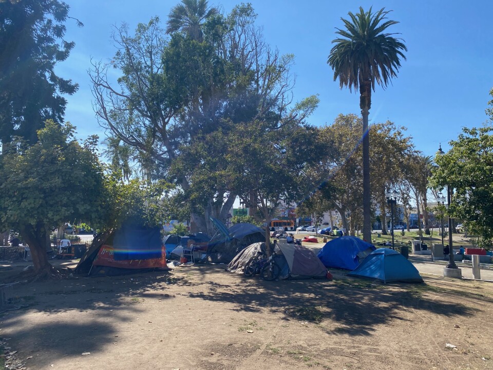Several tents are seen in a shaded area under trees inside MacArthur Park. 