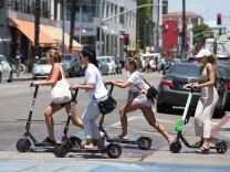 Young women ride shared electric scooters in Santa Monica, California, on July 13, 2018. - Cities across the U.S. are grappling with the growing trend of electric scooters which users can unlock with a smartphone app. Scooter startups including Bird and Lime allow riders to park them anywhere that doesn't block pedestrian walkways but residents in some cities, including Los Angeles, say they often litter sidewalks and can pose a danger to pedestrians. (Photo by Robyn Beck / AFP)        (Photo credit should read ROBYN BECK/AFP/Getty Images)