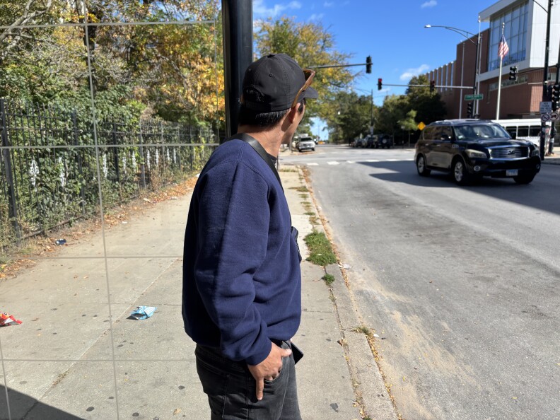 A man's head is turned away from the camera as he stands on a sidewalk.