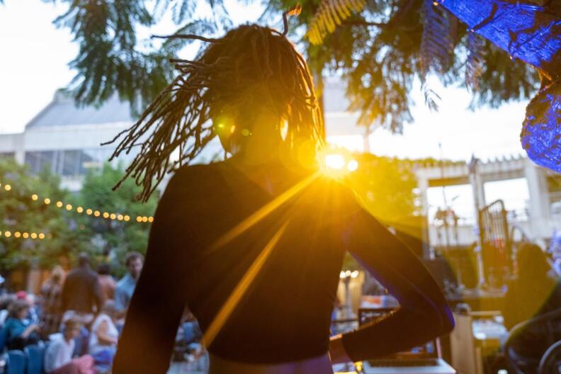 Back silhouette of a woman with dreads moving around and shaking them in the sunlight.
