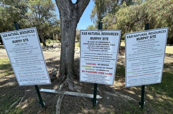 Three signs in English and other languages have warnings about dangerous gas and phone numbers to call in case of an emergency.